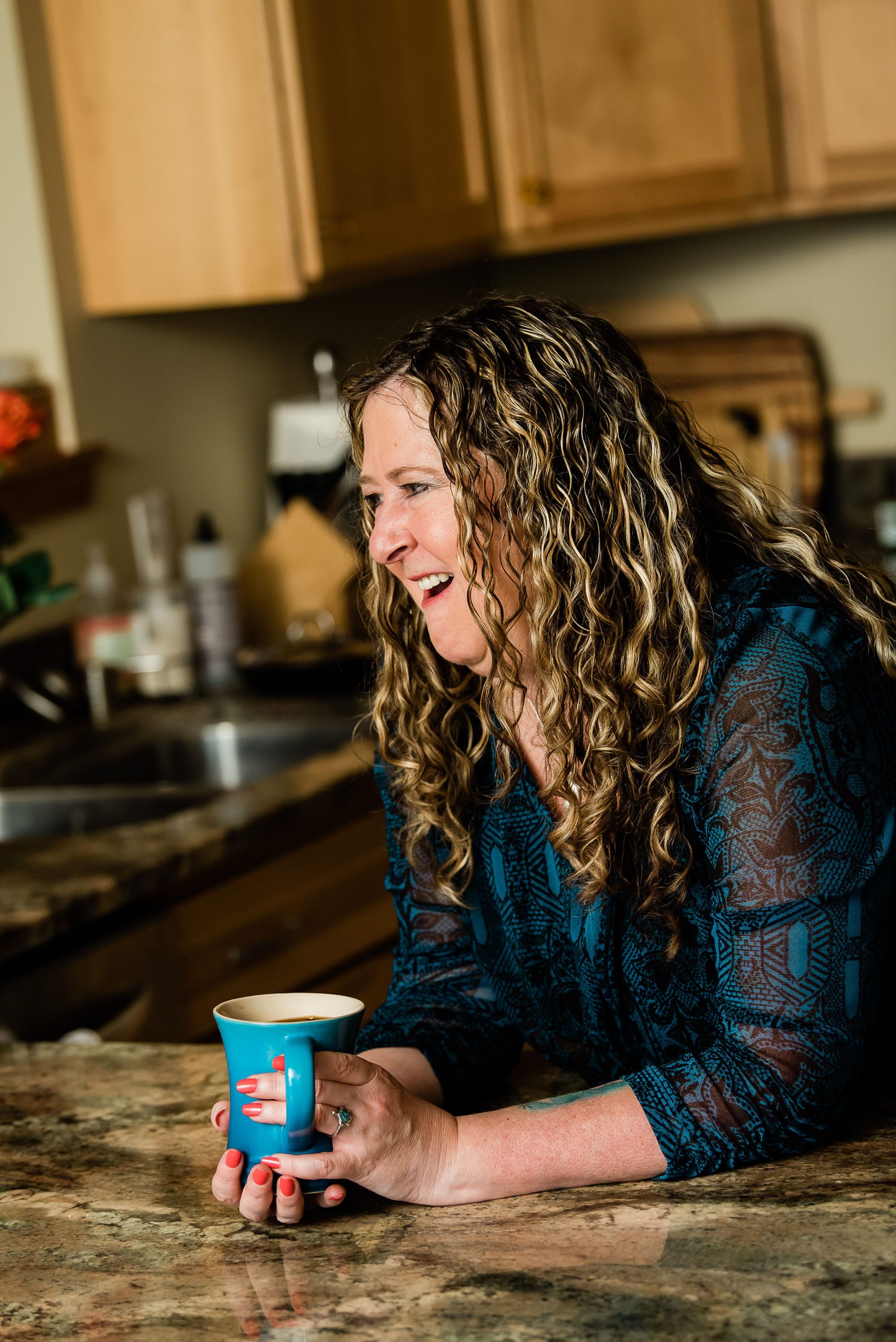 Pam laughing at her kitchen counter with a bright blue coffee mug